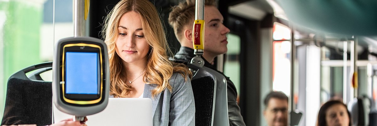 Una ragazza seduta in autobus lavora con il laptop. Sullo sfondo si vedono altri passeggeri.