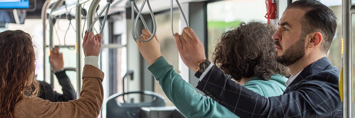 Three passengers are holding on to the handles of the bus