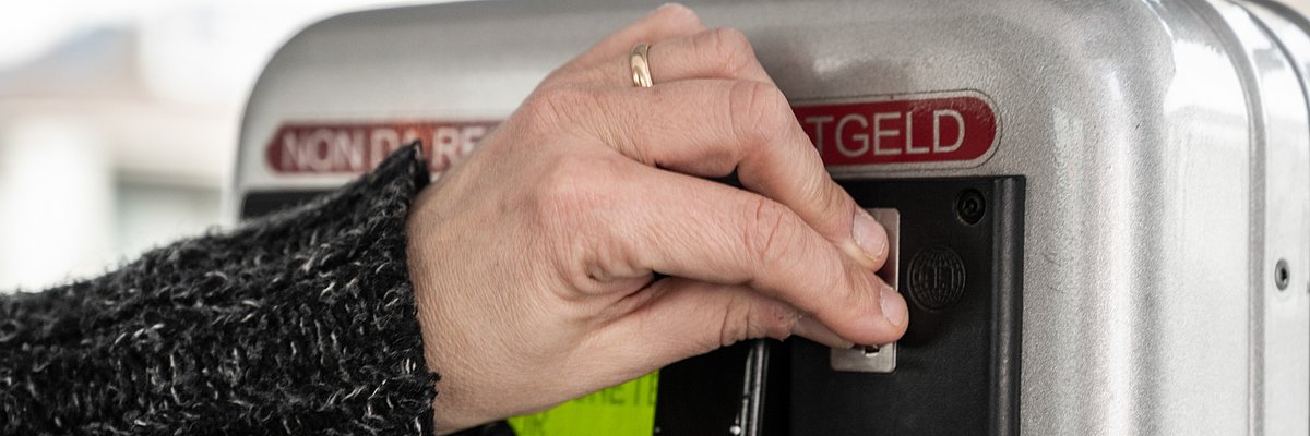 A person is buying a ticket at a ticket machine on the bus. You can see a hand, which is inserting a coin in the machine.