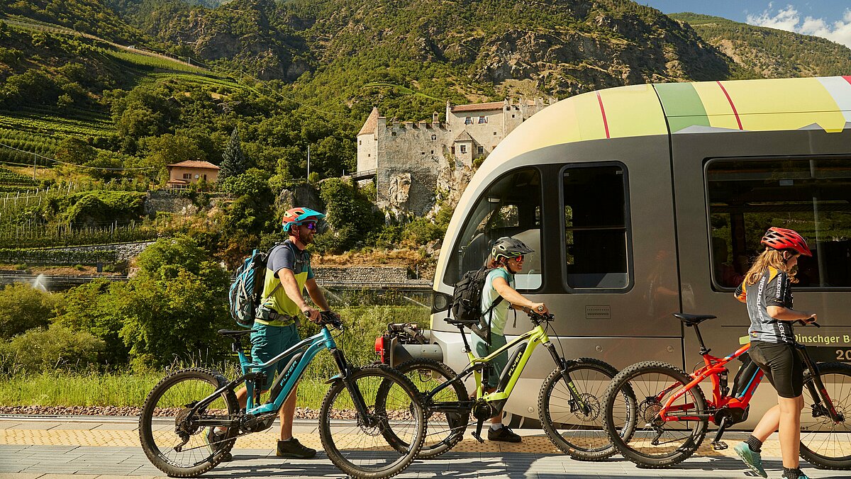 Alcuni turisti in bicicletta davanti a un treno della Val Venosta